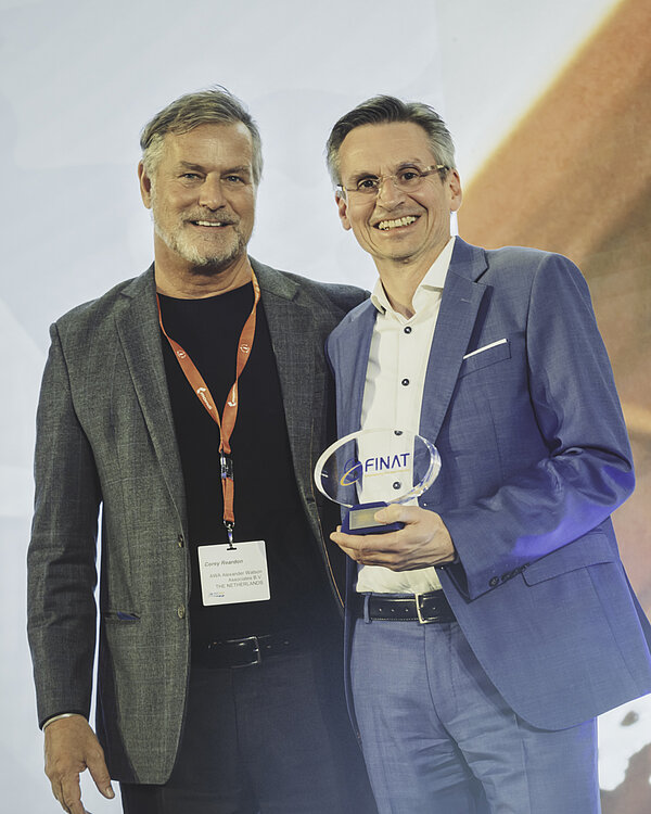 Branchenexperte Corey Reardon, CEO des Marktforschungs- und Beratungsunternehmens AWA Alexander Watson Associates, überreicht den FINAT-Innovationspreis an Dr. Jens Vor der Brüggen, Leiter Forschung + Entwicklung bei der Schreiner Group.
