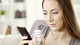 Frau mit Handy und Medikament 