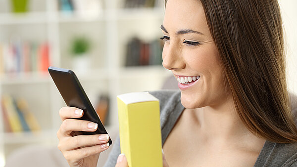Frau liest mit Smartphone digital übermittelte Informationen von einer Medikamentenschachtel aus.