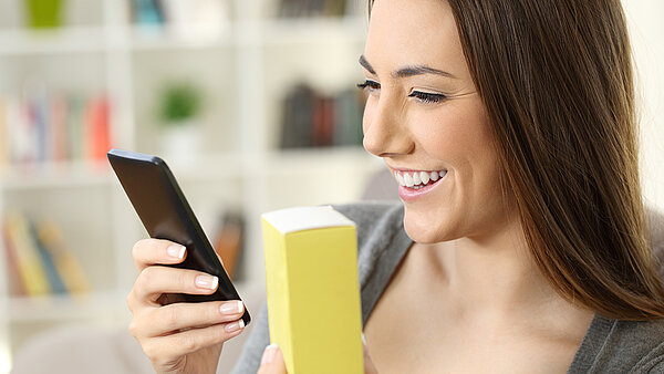 Woman uses smartphone to read digitally transmitted information from a medicine box.