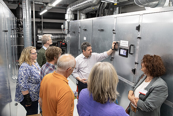 Sebastian Krause aus dem Facility Management erläutert den Besuchern die digitale Anzeige am Wärmepumpensystem.